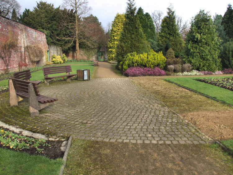 Cobbled crescent in walled garden with benches overlooking flower beds